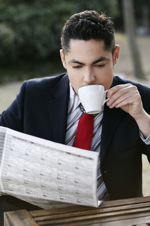 Businessman drinking coffee while reading newspaperの写真素材