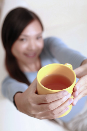 Woman enjoying a cup of tea while relaxing on the couchの写真素材
