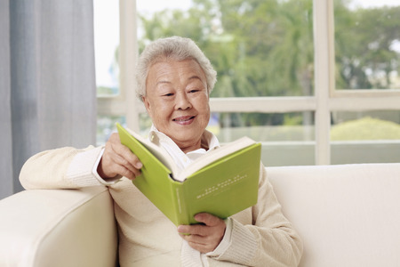 Senior woman sitting on the couch reading bookの写真素材