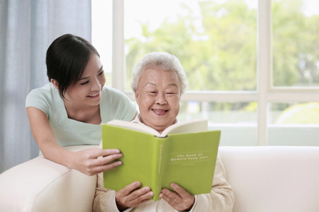 Senior woman and woman reading book togetherの写真素材