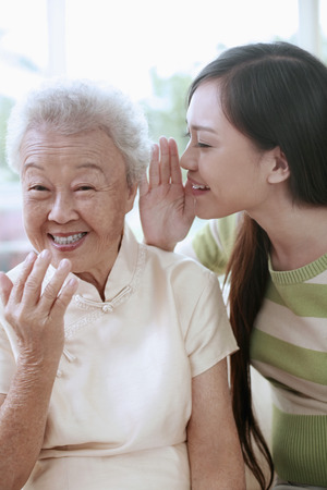 Woman whispering into senior woman's earの写真素材