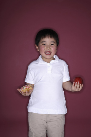 Boy holding doughnut and apple in each handの写真素材