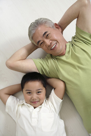 Senior man and boy lying on the floor, smilingの写真素材