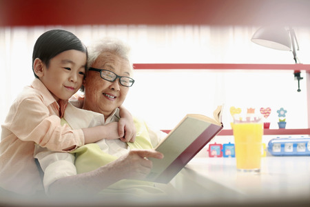 Boy and senior woman reading book togetherの写真素材