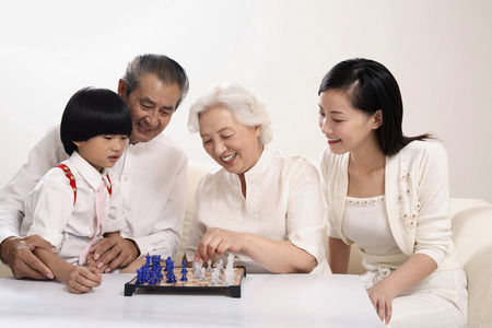 Boy playing chess game with senior woman, woman and senior man watching