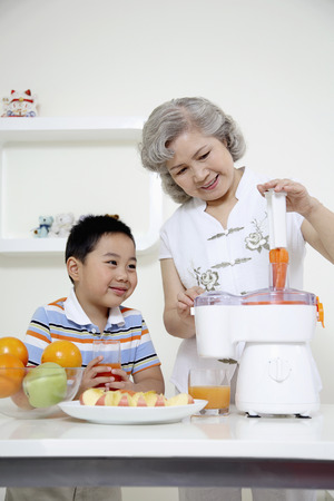 Senior woman putting carrots into juicer, boy watchingの写真素材