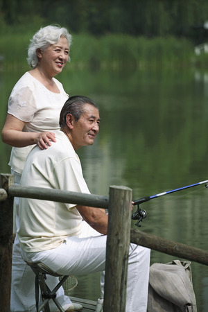 Senior man fishing on a dock, senior woman standing beside himの写真素材