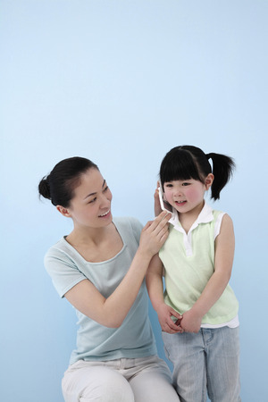 Woman holding cell phone at girl's earの写真素材