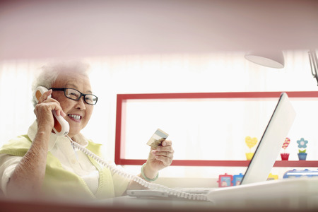 Senior woman talking on the phone while holding credit card