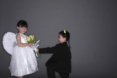 Boy with tuxedo and devil horns giving flowers to girl wearing white dress and angel wingsの写真素材