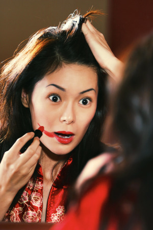 A woman in oriental bathrobe overdrawing her lipstick out of her lipsの写真素材