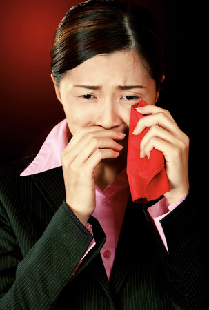 A lady in formal suit wiping her tears with a red handkerchiefの写真素材