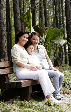 A young boy sitting on the bench with his mother and grandmother の写真素材