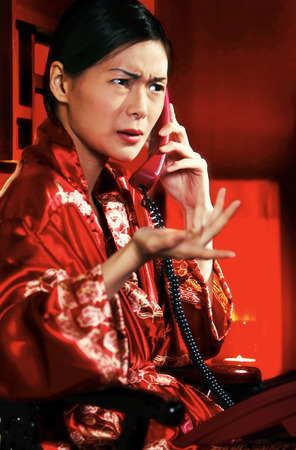 An angry looking woman in oriental bathrobe talking on the phoneの写真素材