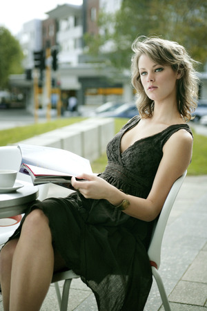 A teenage girl reading a magazine at an open air cafe, posing for the cameraの写真素材