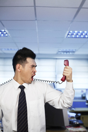 Businessman shouting into a telephone receiverの写真素材