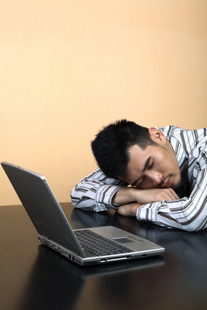 Businessman sleeping with his head on the table and a laptop by his sideの写真素材