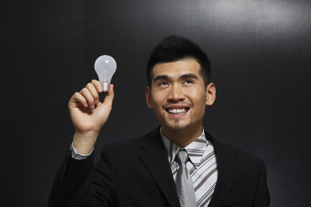 Businessman looking up smiling while holding a light bulbの写真素材
