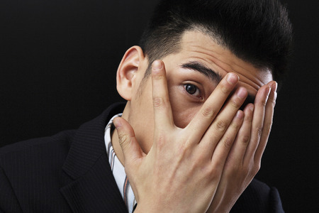 Businessman covering his face, peeping in between his fingersの写真素材