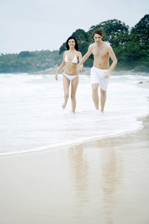 Couple holding hands while running on the beachの写真素材