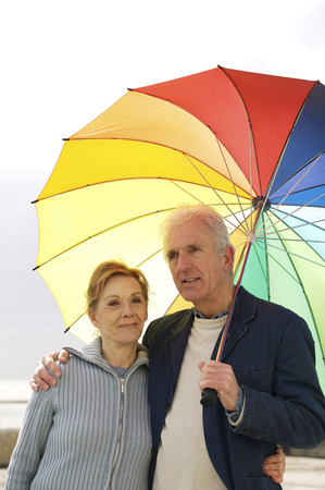 A man having his arms around his wife, holding an umbrellaの写真素材