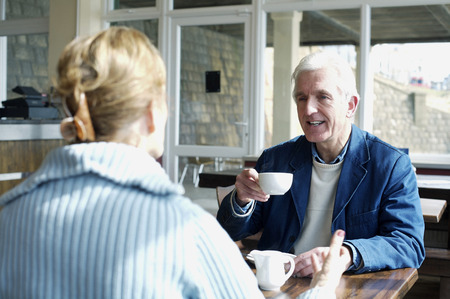 A man lifting a cup of coffee while talking to his wifeの写真素材