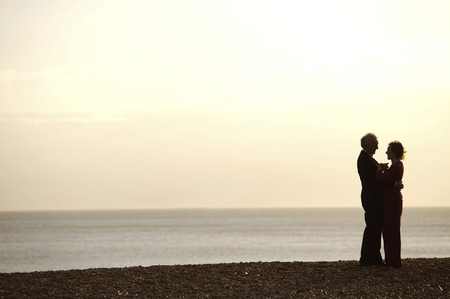 An elderly couple hugging face-to-face on the beach, during sunsetの写真素材