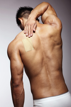 Man putting pain relief patch on his backの写真素材