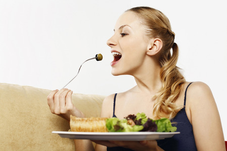 Woman enjoying a plate of quiche with garden salad and fresh herbsの写真素材