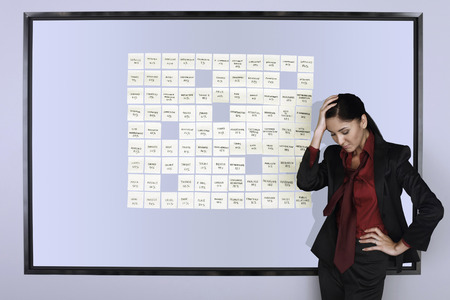 Businesswoman with hand on head contemplating beside wall of adhesive notes