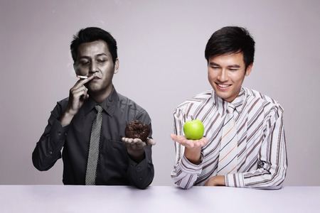 Businessman smoking while holding rotten apple, another businessman holding a fresh green appleの写真素材