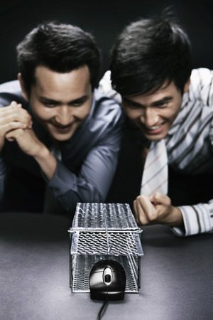 Businessmen watching in excitement as computer mouse getting out from a mouse trapの写真素材