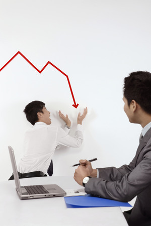 Businessman trying to prevent line graph from going downの写真素材