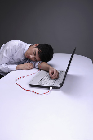 Businessman transferring blood from his hand to laptop through IV drip tube, head lying on the tableの写真素材