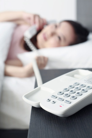 Woman lying down on the bed while talking on the phone, focus on foregroundの写真素材