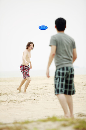 Men playing with flying disc on the beachの写真素材