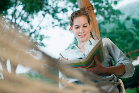 Woman lying in hammock writing diaryの写真素材