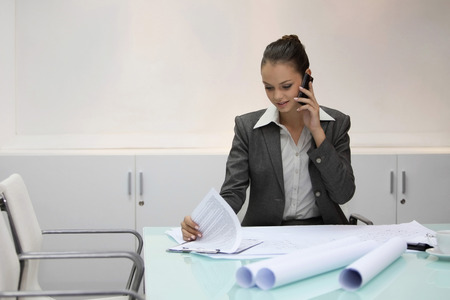 Businesswoman talking on the phone while looking at documentの写真素材