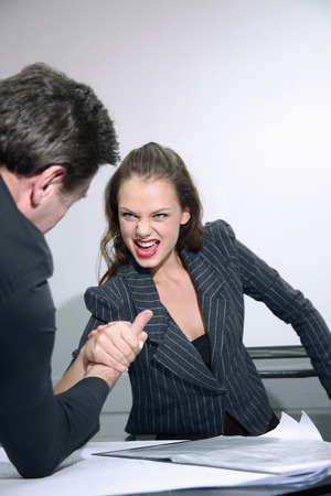Businessman and businesswoman arm wrestling on tableの写真素材