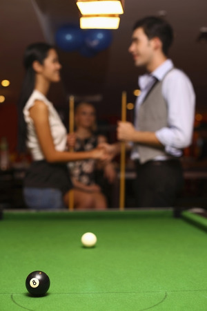 Pool balls on pool table, man and woman shaking hands after the game