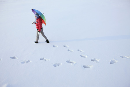 Woman with umbrella walking on snowの写真素材