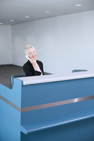 Businesswoman sitting behind ticket counter, talking on the phoneの写真素材