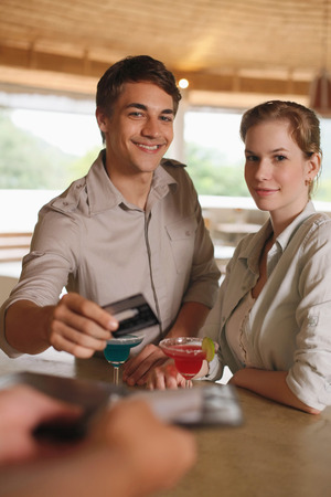 Man and woman drinking at the bar, man paying for the drinksの写真素材