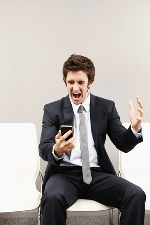 Businessman looking disappointed after reading text messages on mobile phoneの写真素材
