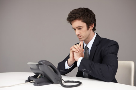 Businessman sitting beside telephone, waiting for phone callの写真素材