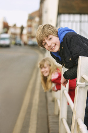 Boy and girl leaning against railing, smiling at the cameraの写真素材