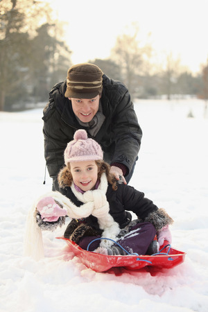 Father pushing daughter on sledの写真素材