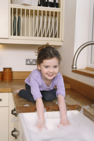 Girl playing with bubbles in the kitchen sinkの写真素材