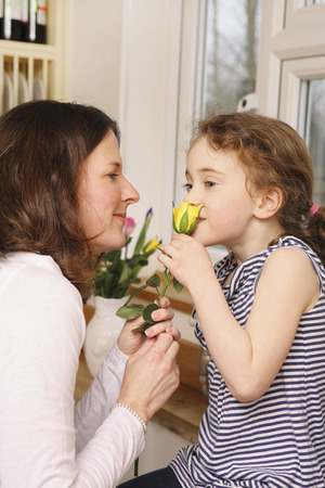 Daughter smelling a flower while mother looks onの写真素材