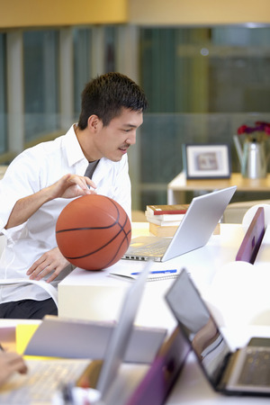 Businessman playing with basketball while looking at laptopの写真素材